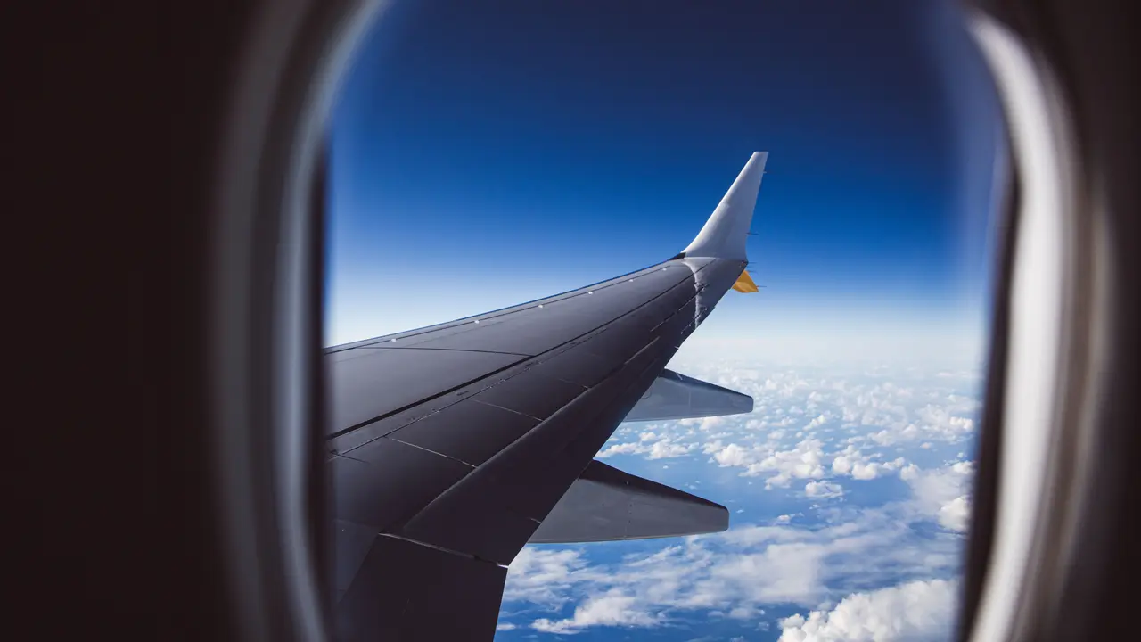 Die Tragfläche eines Flugzeugs über einer geschlossenen Wolkendecke, aufgenommen aus einem Passagierfenster.