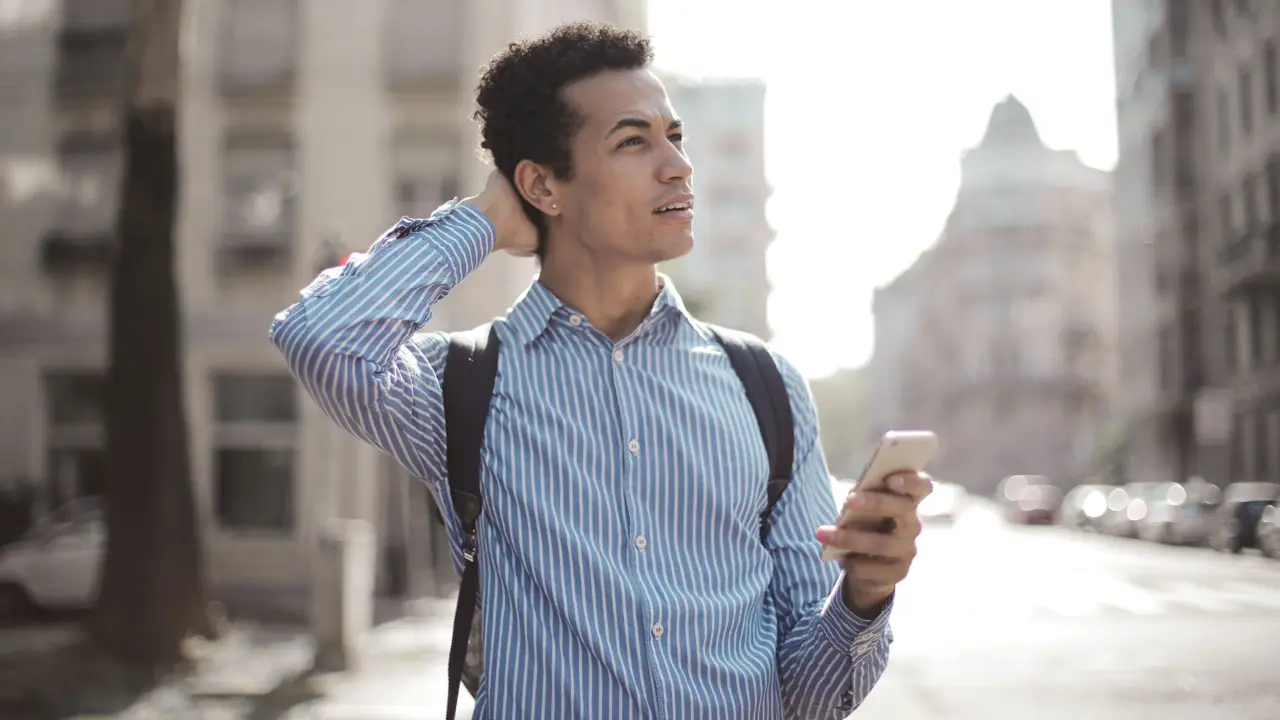 Un uomo fermo in una via di città guarda il telefono con l’aria di chi si è perso.