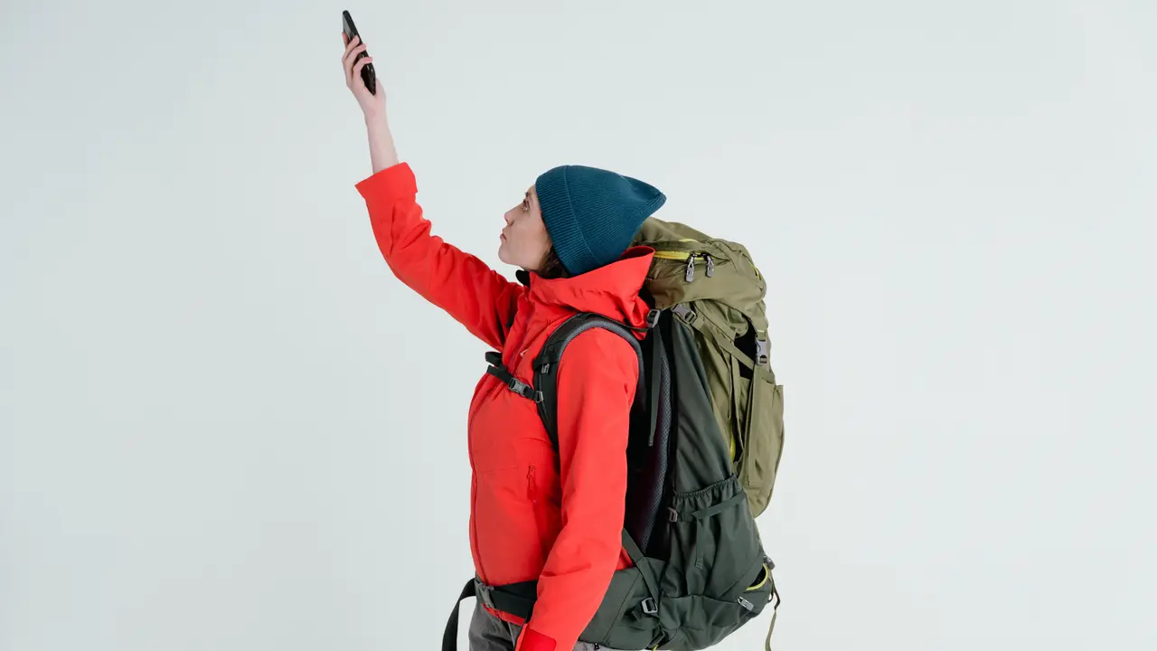 Ein Wanderer in Winterkleidung, den Rucksack auf dem Rücken, hält sein Handy hoch und sucht Empfang.