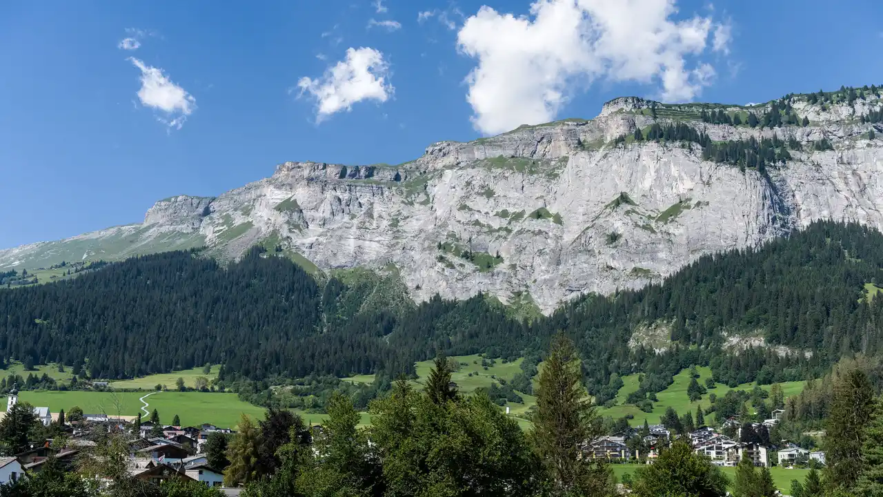 Ein Alpendorf unter steilen grünen Bergen bei klarem Himmel.