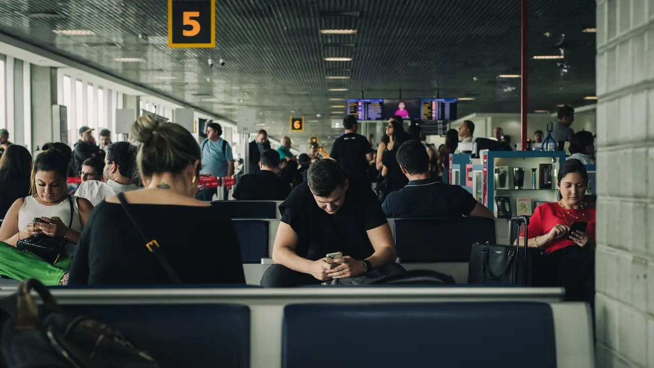 Reisende sitzen mit ihren Handys nebeneinander in einer Wartehalle am Flughafen von São Paulo.