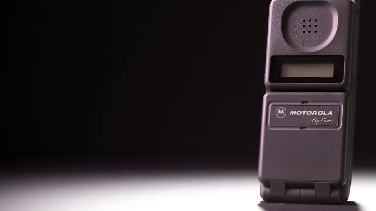 A vintage Motorola flip phone, lit dramatically against a dark background.