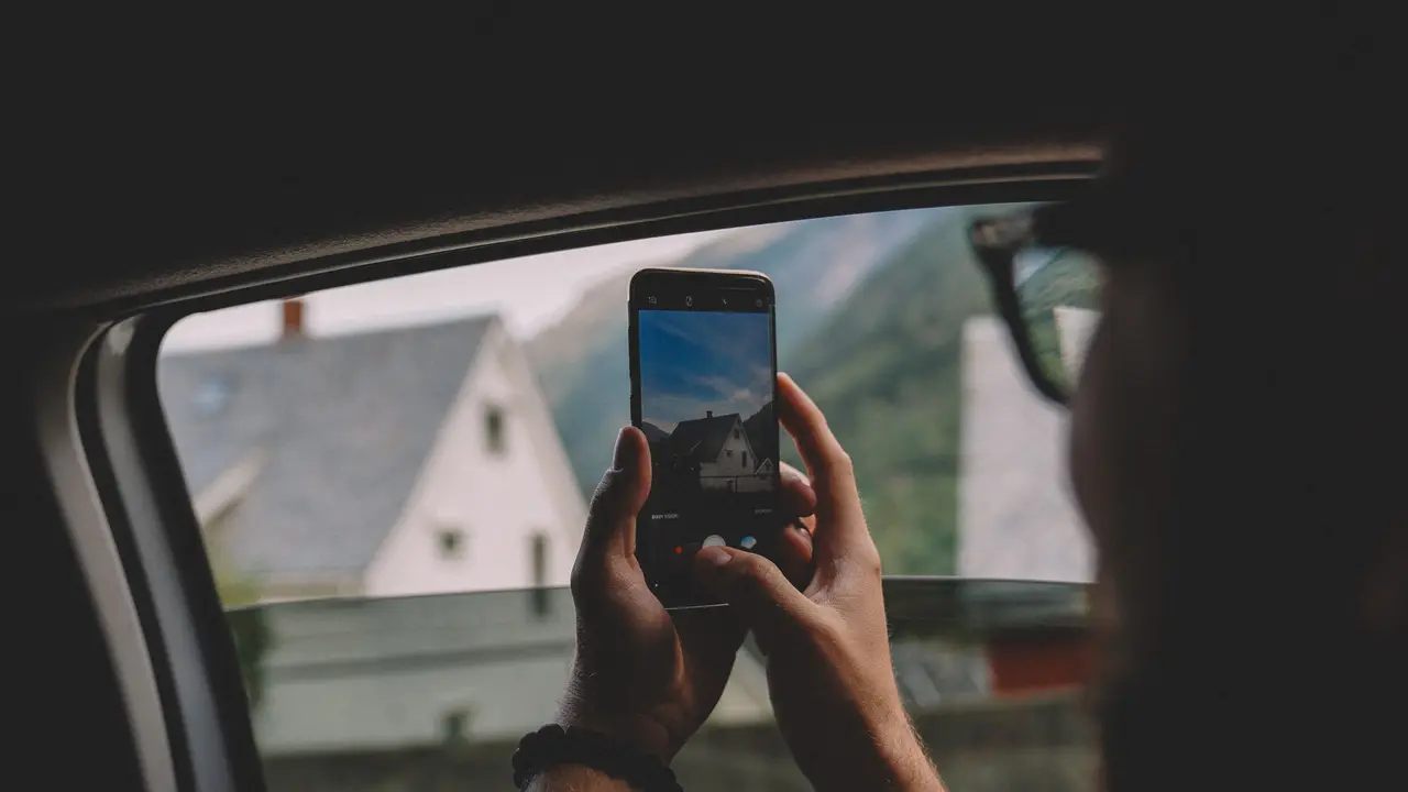 Eine Hand hält ein Handy ans Autofenster und fotografiert eine Fjordlandschaft.