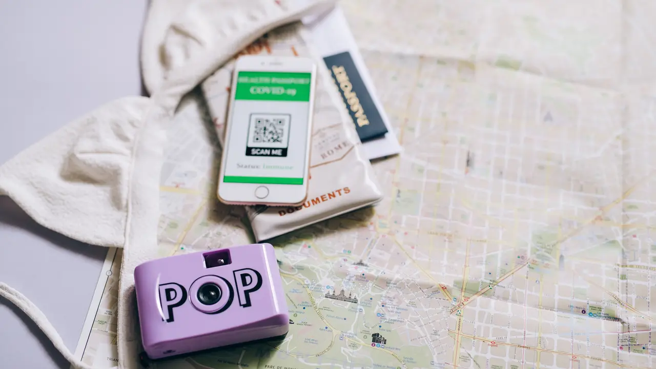Un passeport, une carte routière pliée, un téléphone et un appareil photo compact, posés côte à côte sur une table.