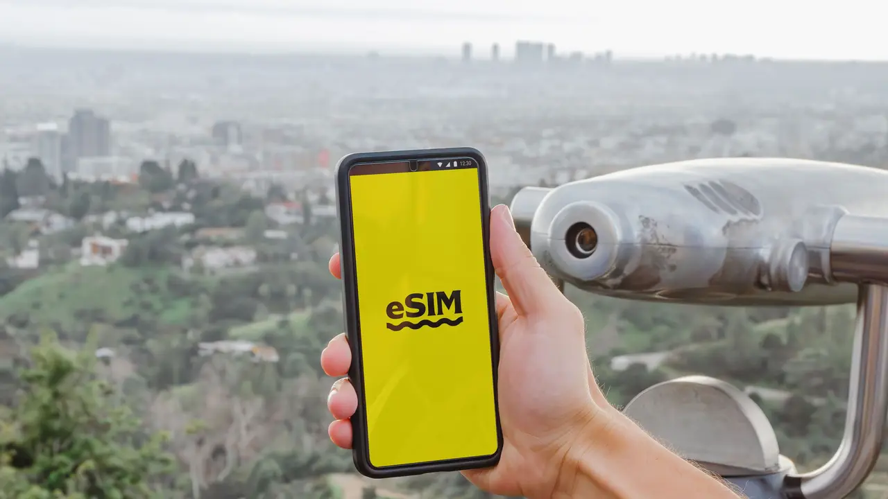 Eine Hand hält ein Handy an einem Aussichtspunkt über einer weit ausgebreiteten Stadt.