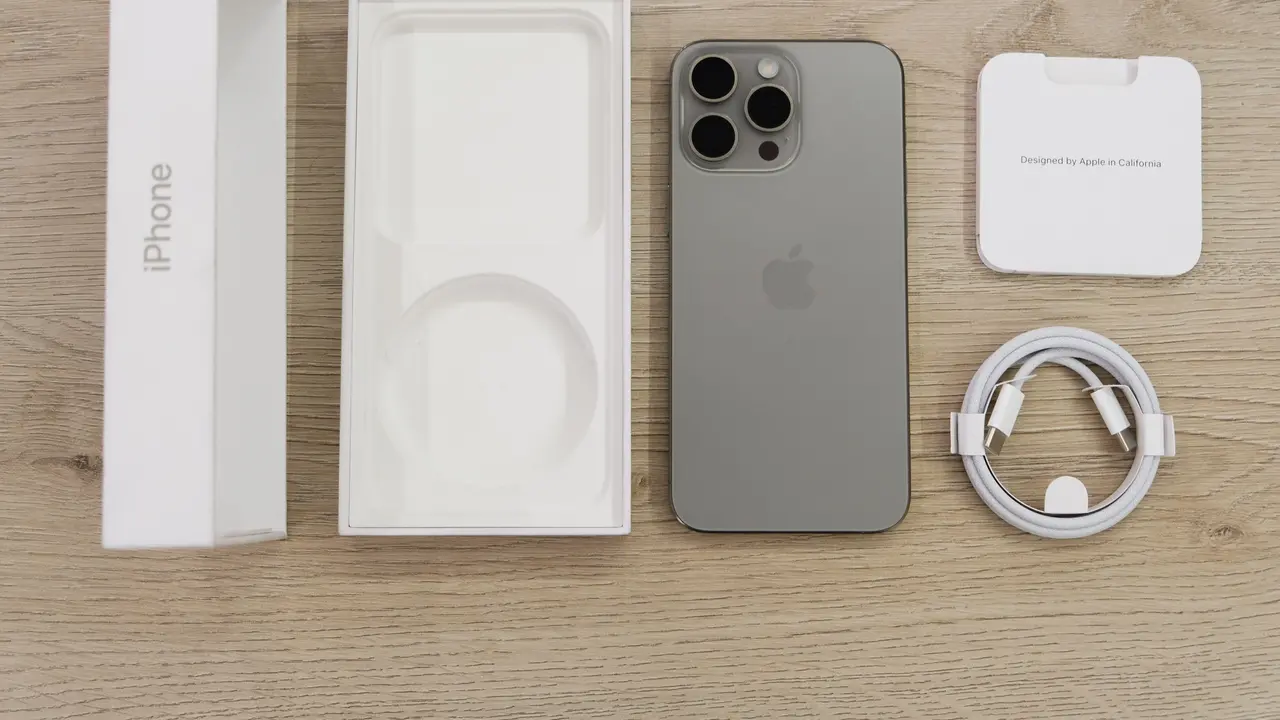 Un iPhone appoggiato su un tavolo di legno, accanto alla sua scatola e agli accessori per caricarlo.