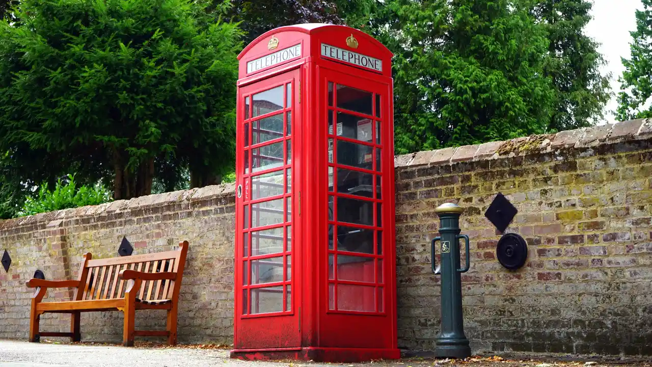 A vintage red telephone booth against a brick wall.