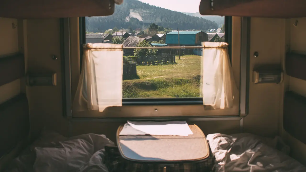 Blick aus dem Fenster eines fahrenden Zuges auf eine Dorflandschaft.