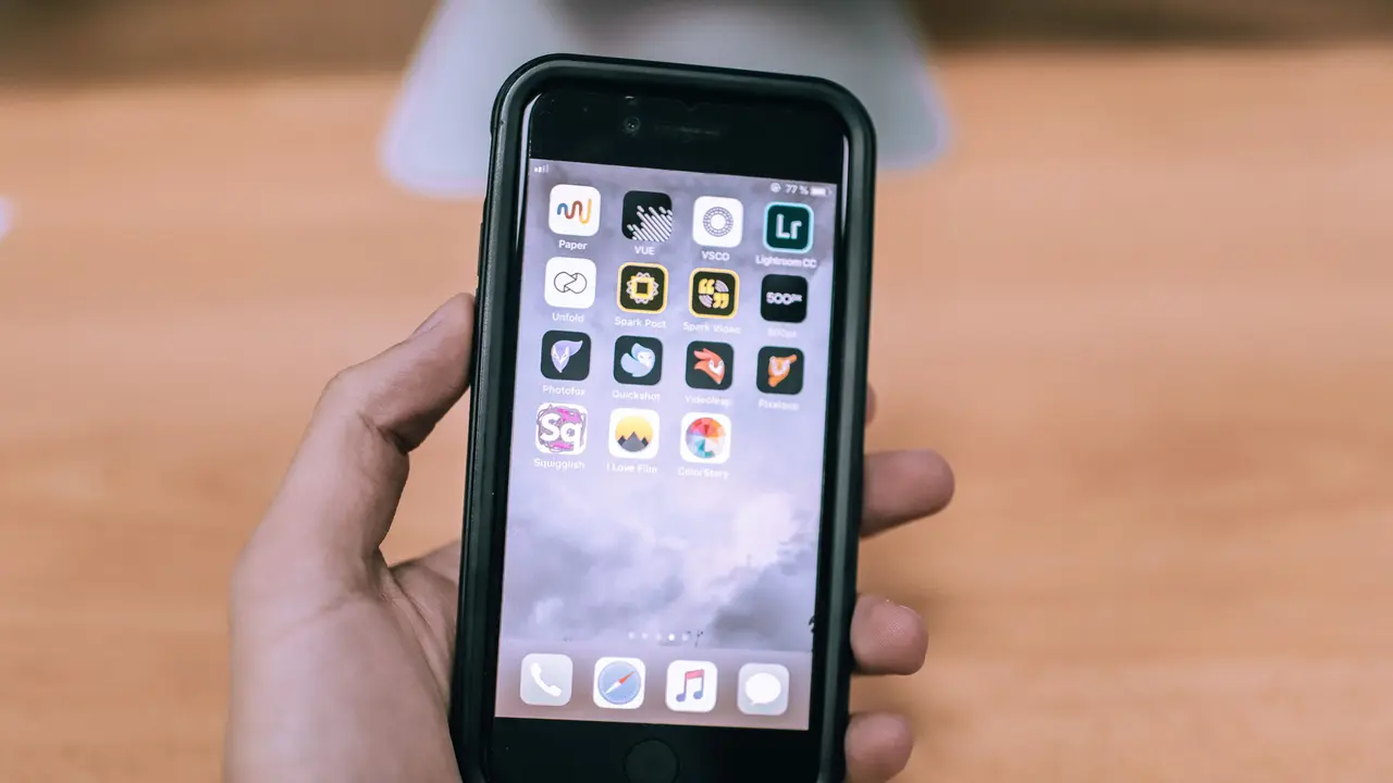Eine Hand hält ein Handy, auf dessen Bildschirm ein Raster aus App-Symbolen zu sehen ist.