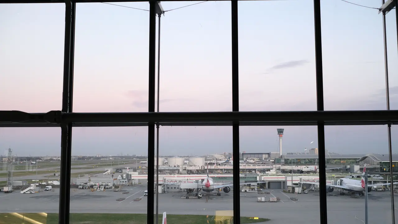 Ein Flugzeug steht in der Dämmerung auf dem Vorfeld in Heathrow, gesehen durch ein Fenster im Terminal.