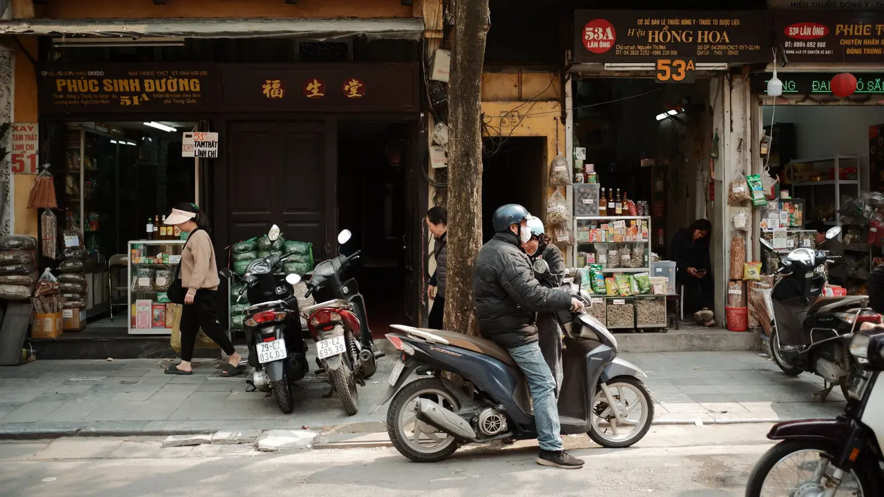 Ein belebter vietnamesischer Straßenmarkt mit Mopeds und offenen Ladenfronten.