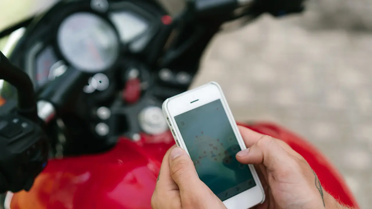 A person on a motorbike checking a map app on their phone.