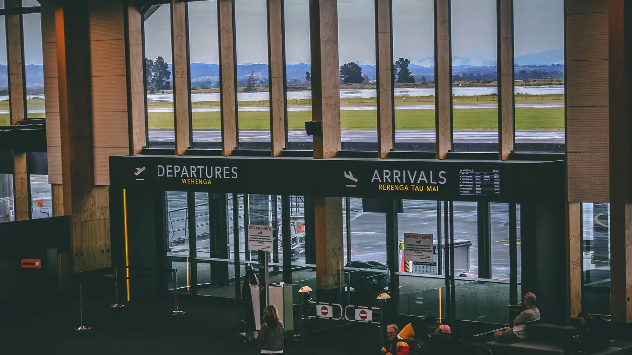 Eine belebte Halle in einem Flughafenterminal, darüber die Anzeigen für Abflug und Ankunft.