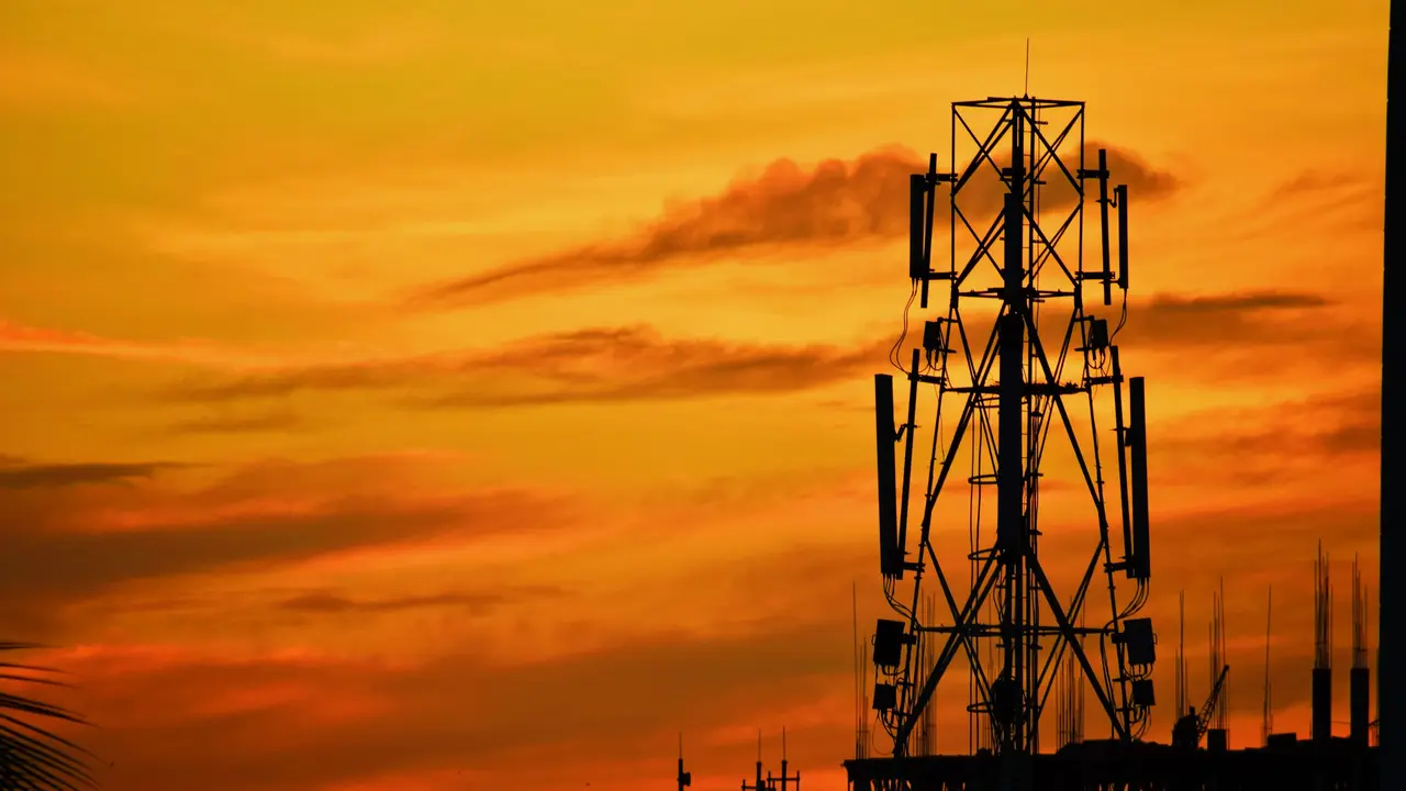 A cellular transmission tower silhouetted against an orange sunset sky.