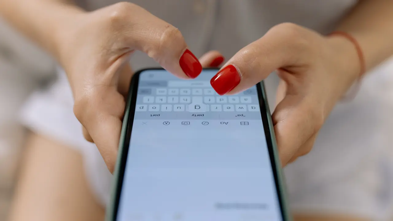 Primo piano di due mani che reggono uno smartphone, con i pollici fermi sopra la tastiera numerica visualizzata sullo schermo.