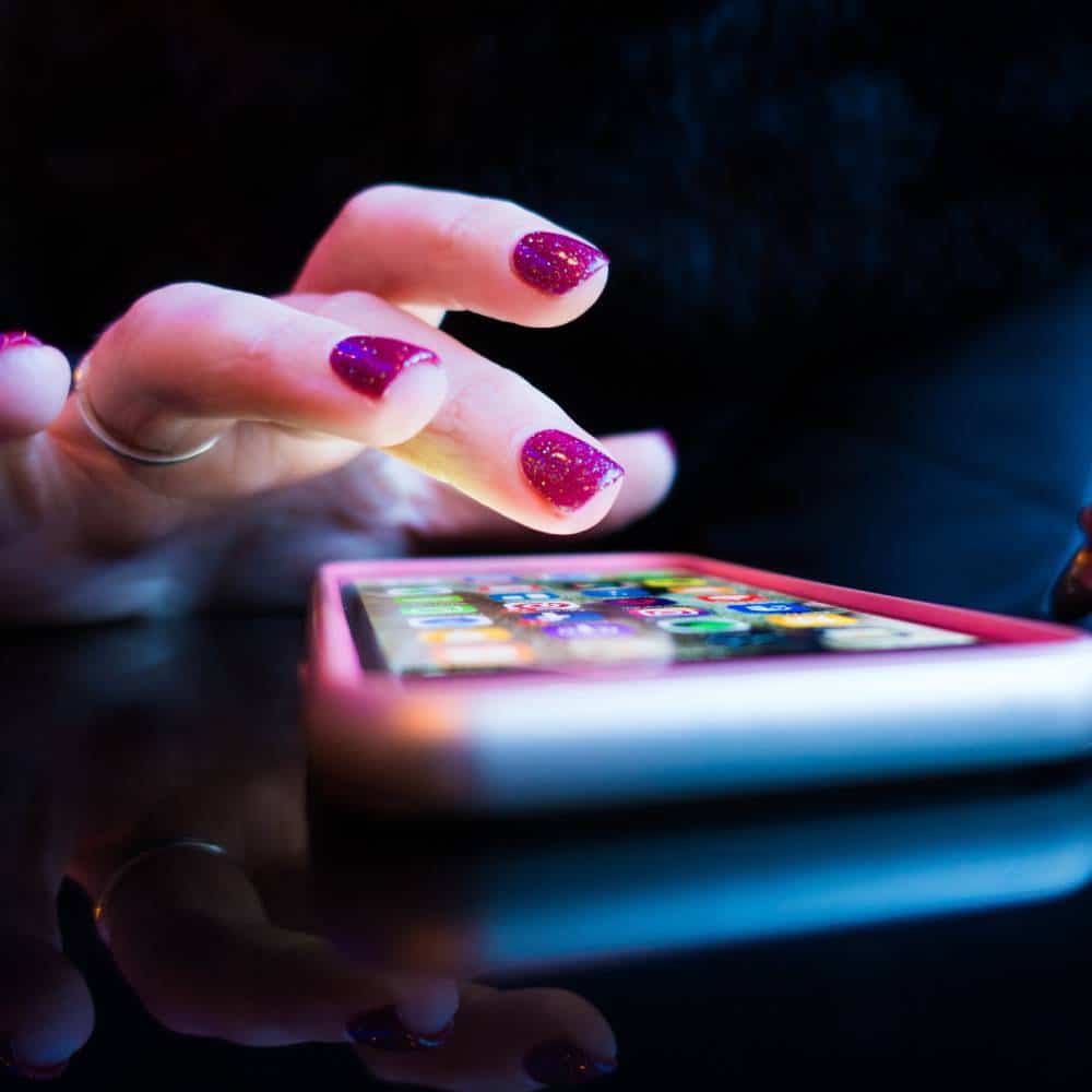 a female hand with pink colored fingernails using a smartphone