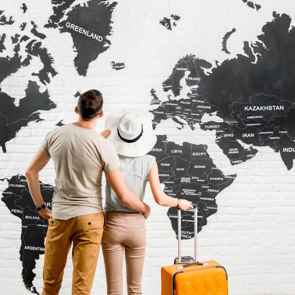a couple holding each other in arms is looking at a wall which has the world map painted on.